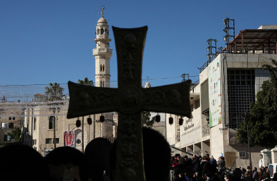 A mosque's minarate is pictured behind a cross during celebrations of Orthodox Christmas outside the Church of the Nativity in the biblical West Bank town of Bethlehem, the traditional birthplace of Jesus Christ, on Jan. 6, 2022.
